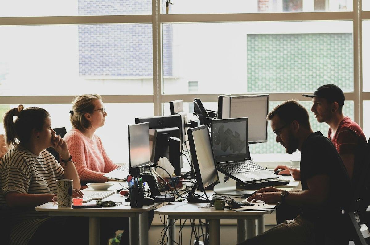 A room of people at desktop machines, daylight coming in from a tall window